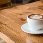 Close-up of a white cup of latte with artistic foam on a rustic wooden table.